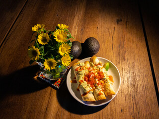 Flautas on white plate with flowers and avocado