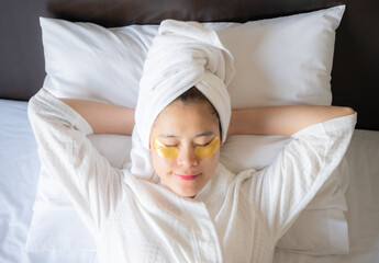 Fototapeta na wymiar Young Asian woman sleeping on bed while sticking under-eye masks for puffiness, dark circles, and wrinkles her under-eyes. Conceptual of woman applying cosmetic product to her face.