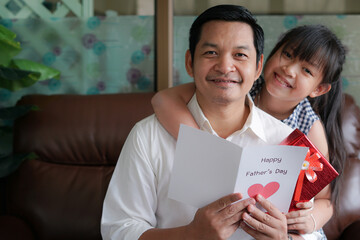 Asian little child daughters congratulating dad and giving him postcard and gift box with smiling and hugging.Concept of Happy father's day