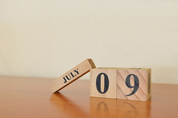 July 9, Date design with calendar cube on wooden table and white background.