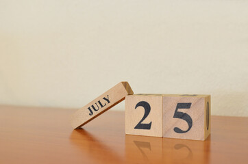 July 25, Date design with calendar cube on wooden table and white background.