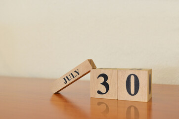 July 30, Date design with calendar cube on wooden table and white background.