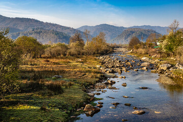 river flowing through misty mountain valley covered with dense forests and blue sky at dawn