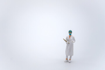 Healthcare concept. Closeup of female doctor miniature figure people wearing surgical face mask and hat with patient files standing on white background.