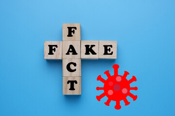 A picture of wooden block written fake fact and coronavirus symbol. People still belief Covid-19 is...