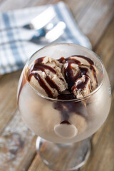 A closeup view of a glass of chocolate ice cream, with chocolate syrup.