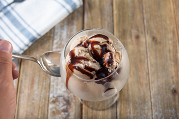 A top down view of a hand with a spoon next to a glass of chocolate ice cream.