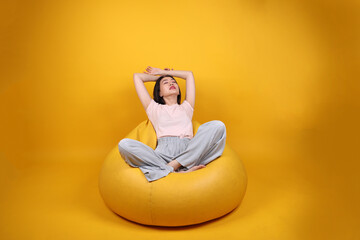 Beautiful young south east Asian woman sits on a yellow beanbag seat orange yellow color background pose fashion style elegant beauty mood expression rest relax exercise stretch yoga