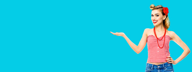Amazed happy woman holding, giving something. Excited girl in pin up, showing product or copy space for some text. Retro fashion and vintage. Aqua blue color background.