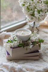 Fresh Spring blossom with a cup of coffee near window with raindrops where sheer curtain and string lights are hanging