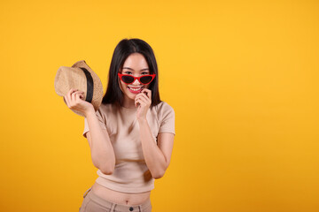 Beautiful young south east Asian woman red frame sunglass hat pose style fashion peak happy on yellow orange background holding hat in hand smile happy