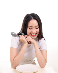 Beautiful young south east Asian woman pretend acting posing holding empty fork spoon in hand eat taste look see white plate on table white background smile happy
