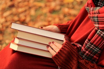Autumn books.Autumn reading. Back to school. School time.Education and knowledge concept.	Stack of books with red cover  in the hands of a girl in an autumn park.