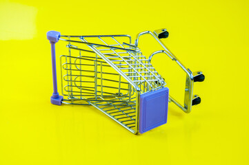 An iron empty grocery cart on a yellow background, turned on its side