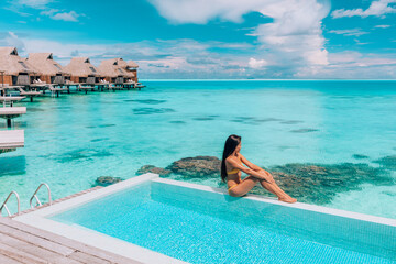 Luxury resort travel vacation destination idyllic overater bungalow villa woman relaxing by infinity pool. Social media influencer traveler luxurious high end lifestyle. - obrazy, fototapety, plakaty