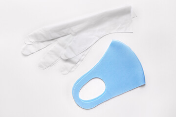 Protective blue face mask with disposable vinyl gloves above white background. Infection prevention during lockdown.