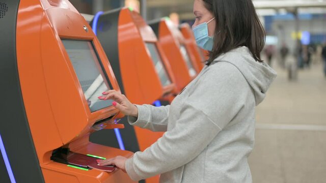 Woman Doing Self-Check In The Airport. woman travel in protective mask using ticket kiosk machine, self check-in at airport terminal, online ticket booking travel