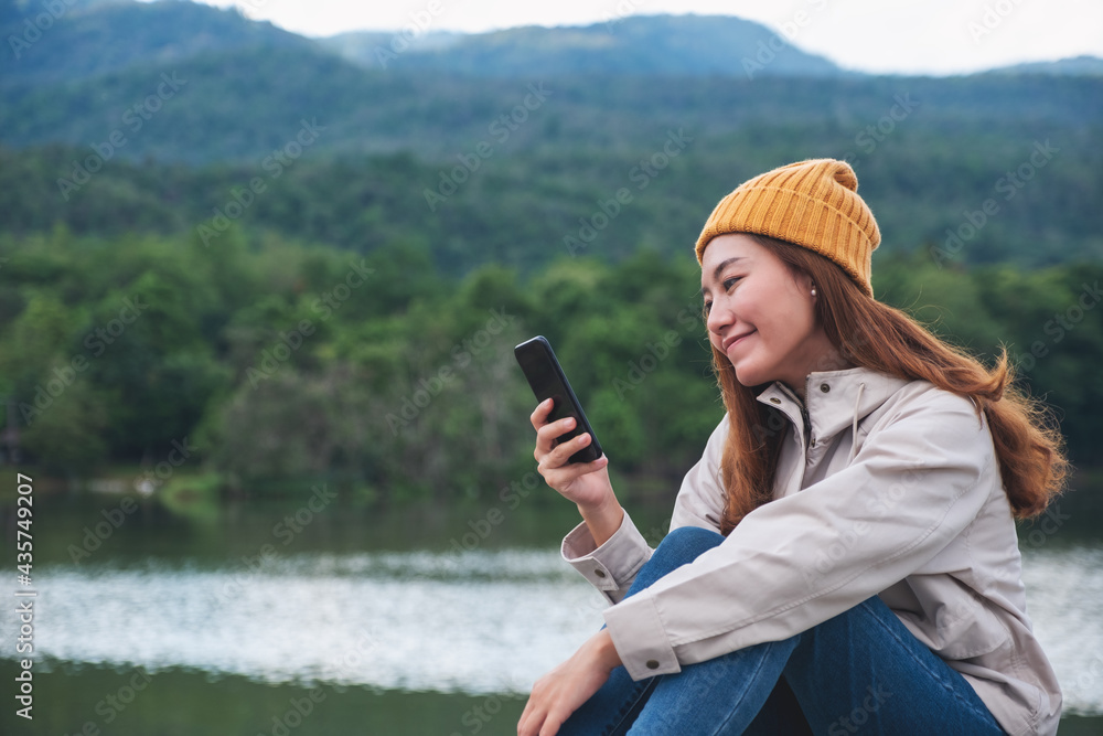 Wall mural a young asian woman holding and using mobile phone while traveling mountains and lake