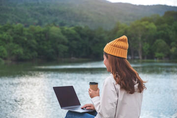 A young woman using and working on laptop computer while traveling mountains and lake