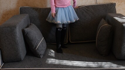 Kid girl in light blue tulle tutu skirt stand on couch with pillows. Legs of girl kid at home