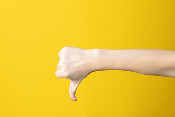 Hand in fist with thumb down gesture on yellow background. Symbol, sign, icon of loss or trouble....
