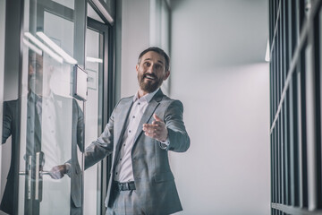 Joyful man in suit gesturing greeting near office door