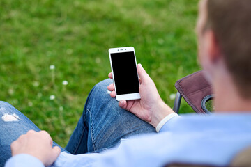 young man freelancer sitting on chair and using smart phone. Remote work and Relaxing in nature. Black screen background place for text