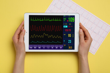 Female hands with heart rate monitor on screen of tablet computer and cardiogram on color background