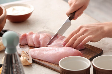 Woman cutting chicken fillet in kitchen, closeup