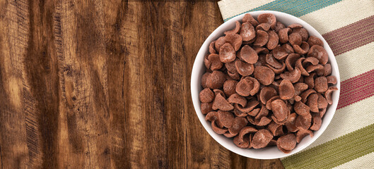 Top view of bowl with sweet chocolate cereal flakes for breakfast on white wooden background