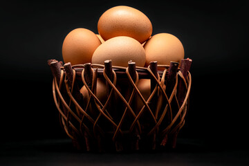 Chicken eggs in basket on dark background.