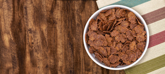 Top view of bowl with sweet chocolate cereal flakes for breakfast on white wooden background
