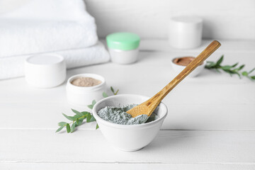 Bowl with cosmetic clay on light wooden background