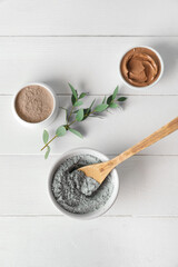 Bowls with cosmetic clay on light wooden background