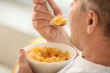 Senior man eating cornflakes at home, closeup