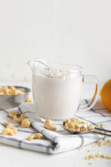 Jug of sour cream with cashew nuts on light background