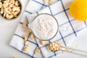 Jug of sour cream with cashew nuts on light background