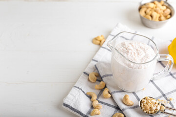 Jug of sour cream with cashew nuts on light background