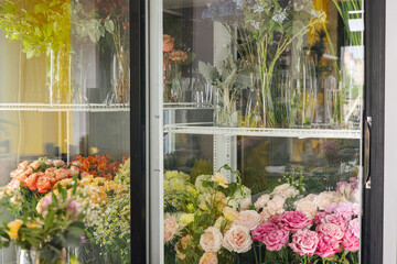 Fresh flowers - pink roses and white eustomas - in front of a floristry shop window, where elegant delicate bouquets stand in anticipation of a buyer