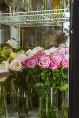 Fototapeta na wymiar Fresh flowers - pink roses and white eustomas - in front of a floristry shop window, where elegant delicate bouquets stand in anticipation of a buyer