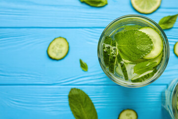 Glass with cucumber lemonade on color wooden background
