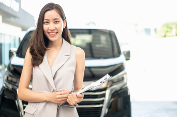 Portrait photo of young professional look Asian automobile sales agent standing in front of new car...