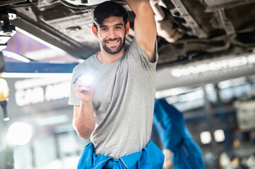 Fototapeta Portrait photo of professional look Caucasian vehicle service technician standing under checking vehicle under body and holding lighting torch in car repair shop. obraz