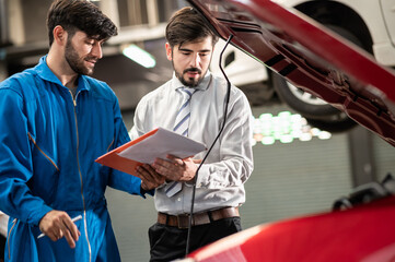 Caucasian car technician or mechanic explaining and showing the checklist or repair items to customer in automobile service center or garage. Car service and vehicle repair concept.