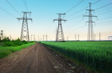 High voltage lines and power pylons in a flat and green agricultural landscape on a sunny day with clouds in the blue sky. Cloudy and rainy. Wheat is growing