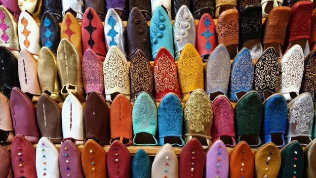 Authentic colorful Moroccan women slippers (babouches) with embroidery, displayed on a wall, in the medina of Marrakech (Marrakesh), Morocco. Camera moves up.