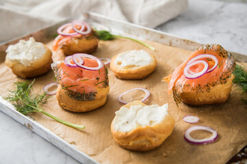 Gravlax Graved Lachs, ein roh gebeizter Fisch mit Dill auf Brötchen mit Frischkäse,  Zwiebelringe auf Backblech mit Backpapier und hell Marmor Hintergrund