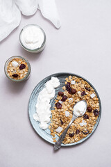 Granola with chia seeds, coconut, dry berries and yogurt in bowls on grey background, copy space. Concept of healthy breakfast menu 