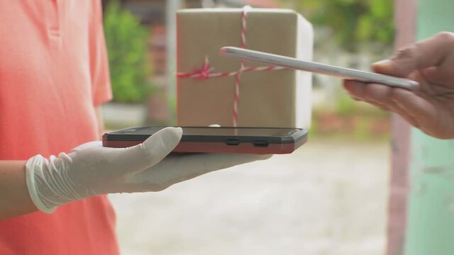 Close up of man's hand receive a parcel cardboard box from a delivery woman and using QR code scan with smartphone for payment. Scanning and paying on mobile device.
