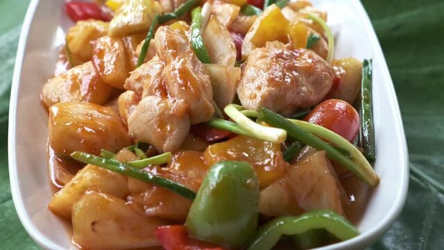 sweet and sour chicken with vegetables in a white dish spinning around